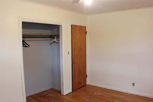 unfurnished bedroom featuring ornamental molding, a ceiling fan, wood finished floors, a closet, and baseboards
