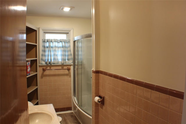 full bathroom with a sink, wood finished floors, tile walls, wainscoting, and enclosed tub / shower combo