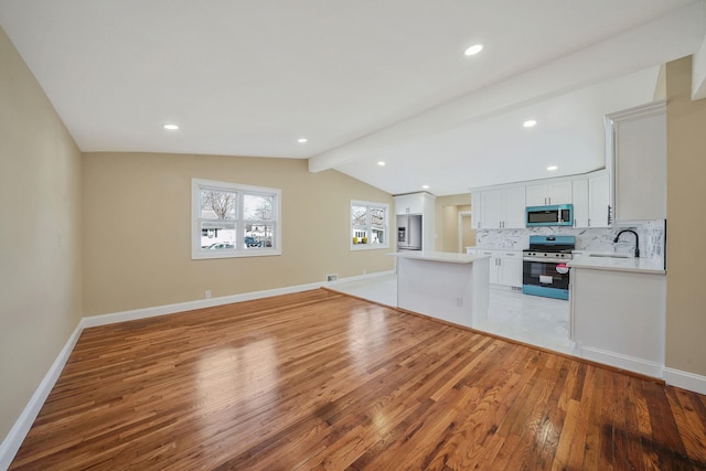 unfurnished living room with light wood-style flooring, a sink, lofted ceiling with beams, recessed lighting, and baseboards