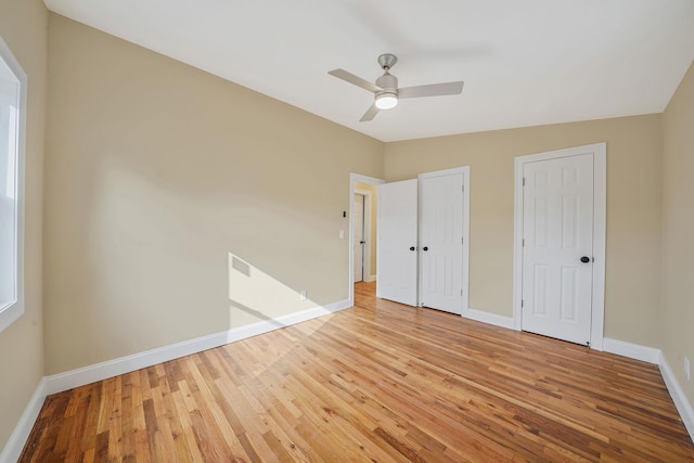 unfurnished bedroom with light wood-style flooring, ceiling fan, baseboards, and multiple closets