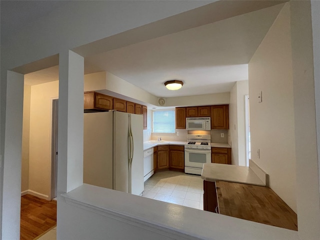 kitchen with white appliances, a peninsula, a sink, light countertops, and brown cabinets