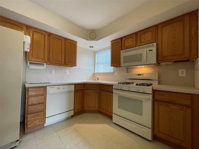 kitchen featuring white appliances, brown cabinetry, light countertops, and a sink