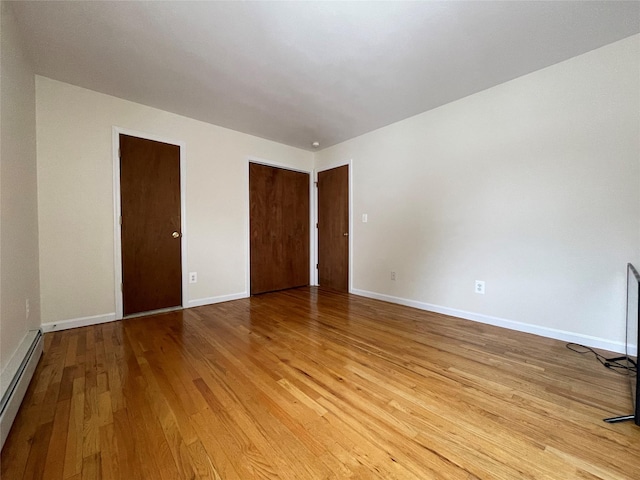 unfurnished room with light wood-type flooring, a baseboard heating unit, and baseboards