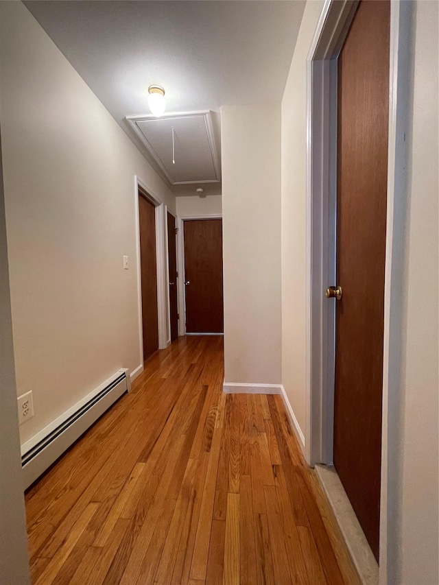 hall featuring baseboards, attic access, a baseboard heating unit, and light wood-style floors