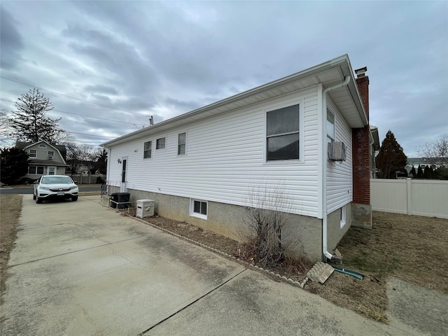 view of property exterior with central AC unit, concrete driveway, a chimney, and fence