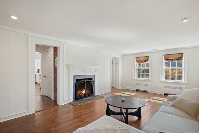 living room featuring a warm lit fireplace, wood finished floors, radiator heating unit, and crown molding