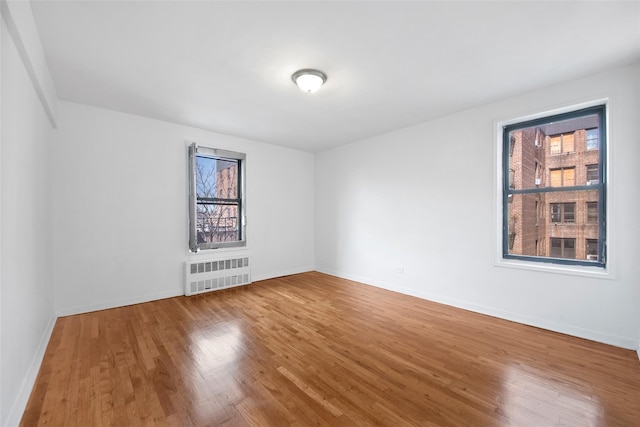 spare room featuring radiator heating unit, baseboards, and wood finished floors