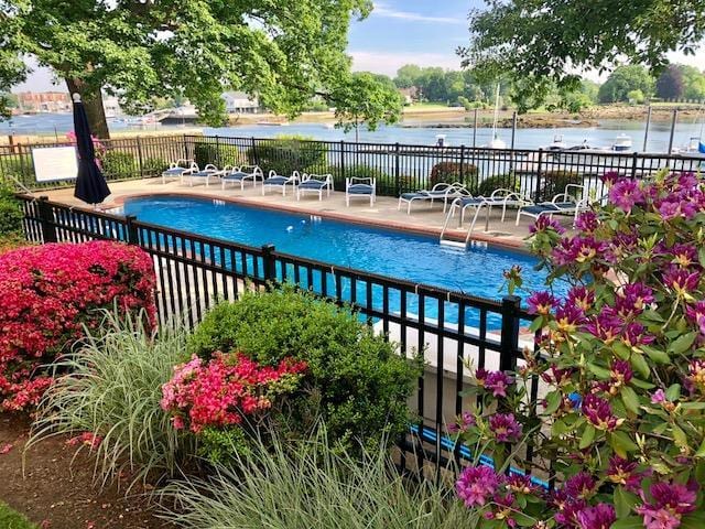 community pool with a water view, a patio area, and fence