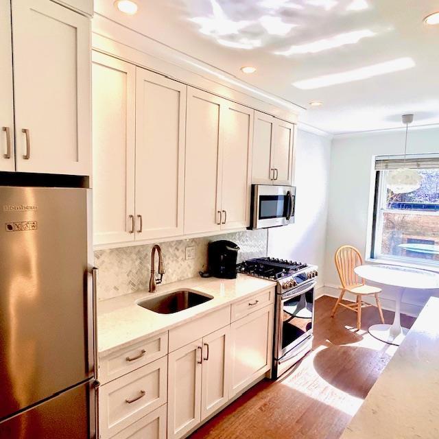 kitchen featuring wood finished floors, a sink, appliances with stainless steel finishes, backsplash, and light stone countertops