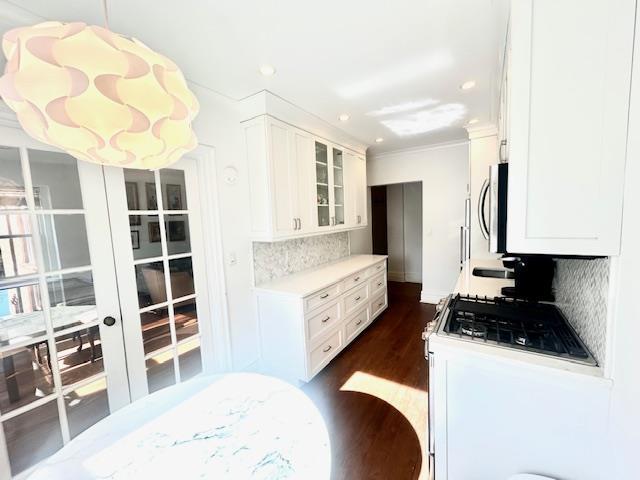 kitchen featuring dark wood-style flooring, light countertops, decorative backsplash, stainless steel microwave, and glass insert cabinets