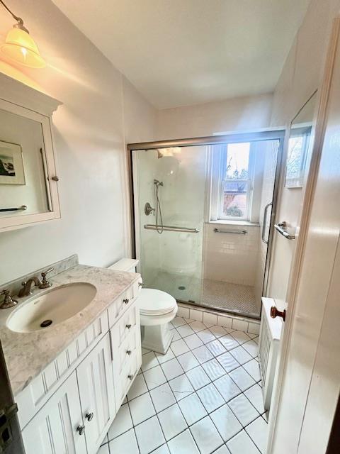 bathroom featuring tile patterned flooring, toilet, a shower stall, and vanity