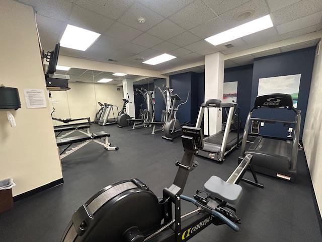 gym featuring a paneled ceiling and baseboards