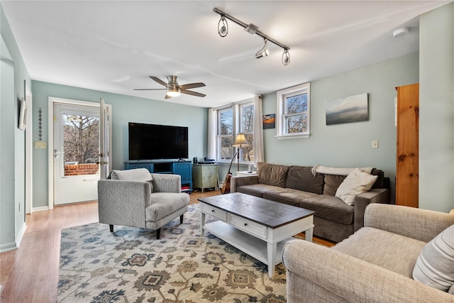 living room featuring wood finished floors, rail lighting, a healthy amount of sunlight, and ceiling fan