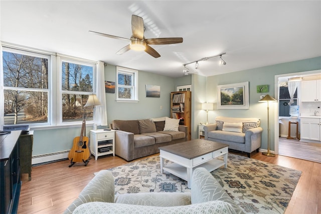 living room featuring light wood-style flooring, baseboards, ceiling fan, and a baseboard radiator