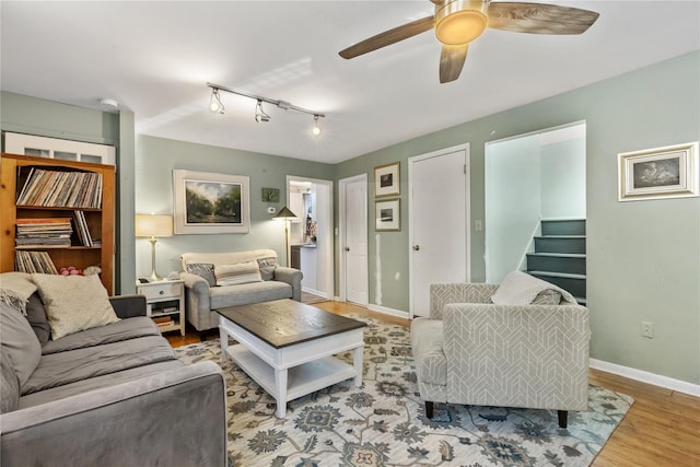 living room with wood finished floors, baseboards, ceiling fan, stairs, and track lighting