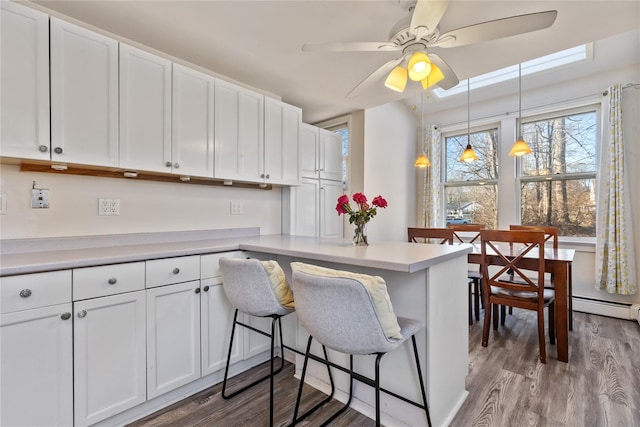 kitchen featuring pendant lighting, wood finished floors, a peninsula, white cabinets, and light countertops