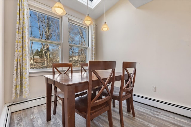 dining space with a skylight, a baseboard radiator, and wood finished floors