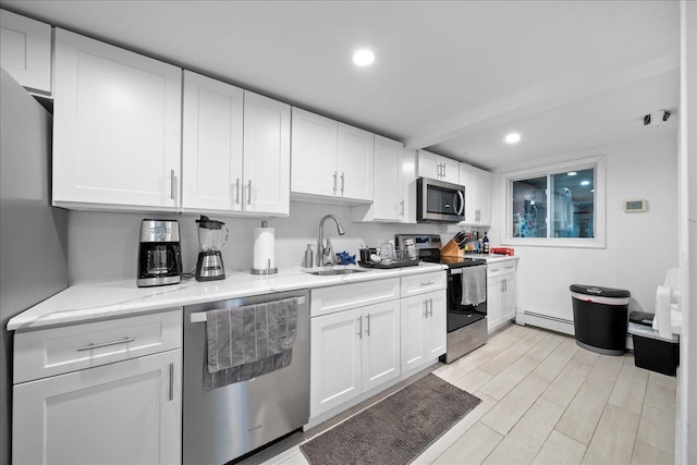 kitchen with stainless steel appliances, a baseboard heating unit, white cabinetry, a sink, and light wood-type flooring