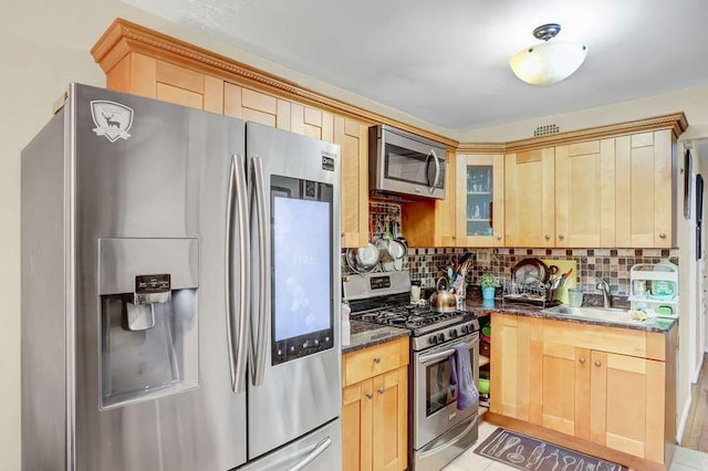 kitchen featuring tasteful backsplash, glass insert cabinets, dark stone countertops, stainless steel appliances, and light brown cabinets