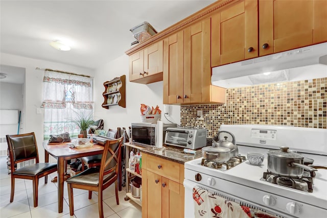 kitchen with light tile patterned flooring, white range with gas stovetop, under cabinet range hood, decorative backsplash, and stainless steel microwave