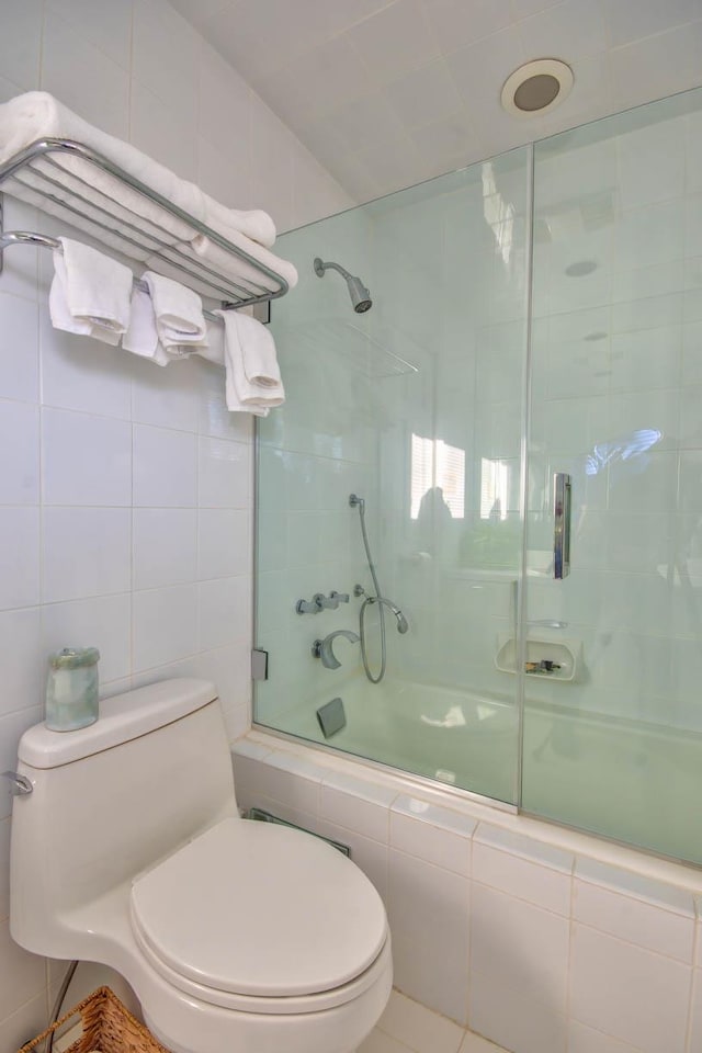 full bathroom with tiled shower / bath, toilet, and tile walls