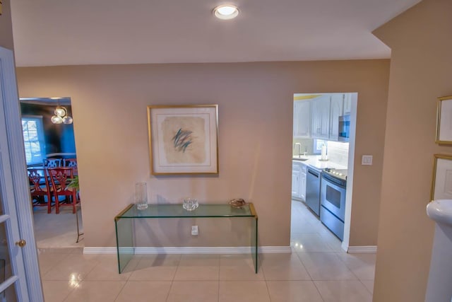 hall featuring light tile patterned floors, baseboards, and a sink