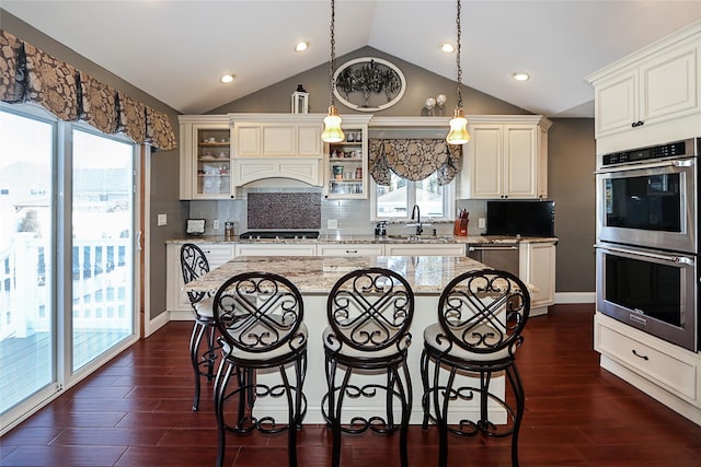 kitchen with a breakfast bar, a sink, dark wood-style floors, appliances with stainless steel finishes, and glass insert cabinets