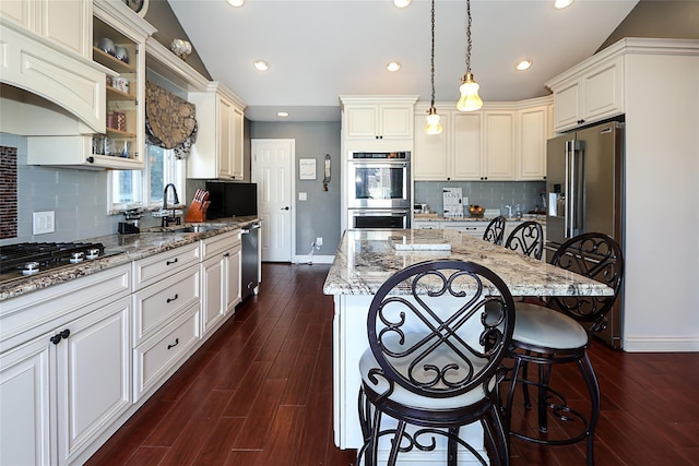 kitchen with light stone counters, dark wood-style flooring, vaulted ceiling, appliances with stainless steel finishes, and a kitchen bar