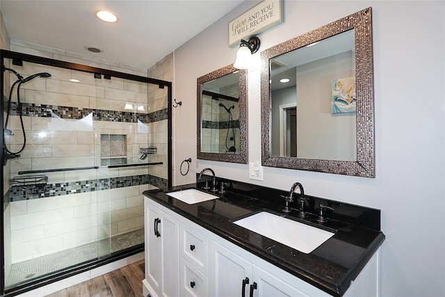 full bath featuring a shower stall, wood finished floors, double vanity, and a sink