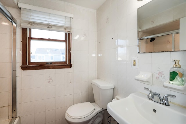 bathroom featuring tile walls, toilet, a shower with door, and a sink