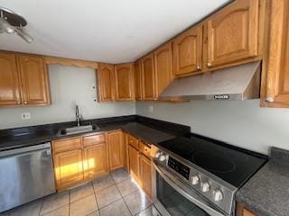 kitchen with under cabinet range hood, stainless steel appliances, a sink, brown cabinetry, and dark countertops