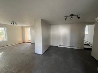 empty room featuring track lighting, a healthy amount of sunlight, and baseboard heating