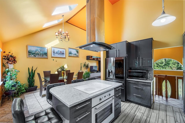 kitchen with a skylight, a notable chandelier, appliances with stainless steel finishes, island range hood, and high vaulted ceiling