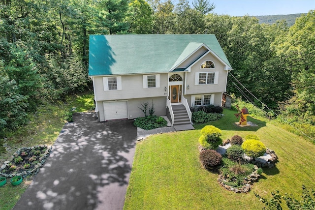 raised ranch with an attached garage, aphalt driveway, and a front yard