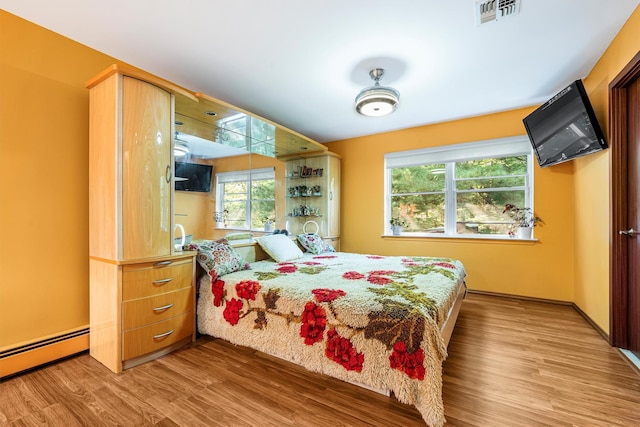 bedroom featuring baseboards, visible vents, baseboard heating, and wood finished floors