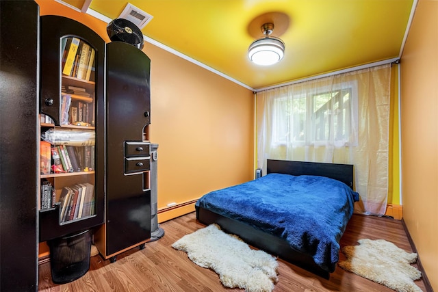 bedroom with a baseboard heating unit, ornamental molding, wood finished floors, and visible vents