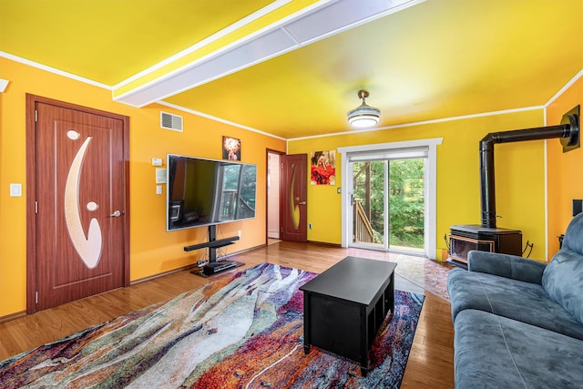 living area featuring wood finished floors, visible vents, baseboards, a wood stove, and crown molding