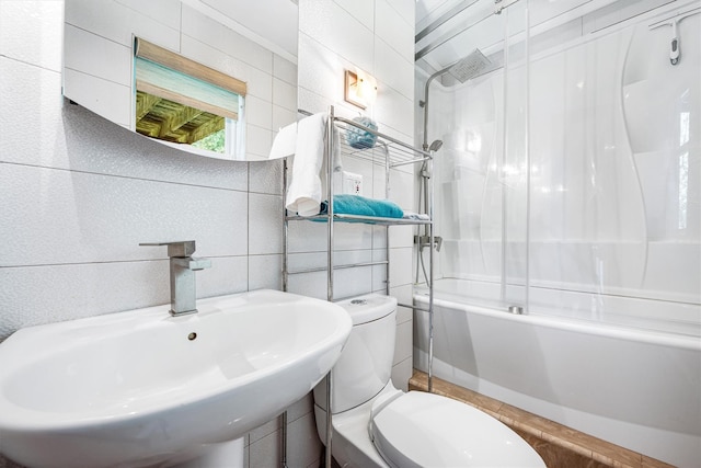 full bathroom featuring toilet, shower / bath combination with glass door, tile walls, and a sink