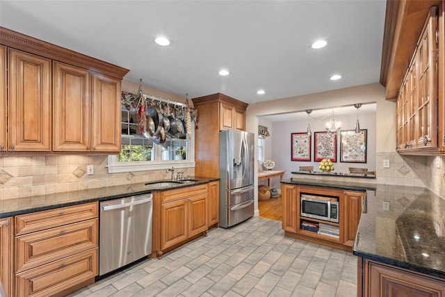 kitchen with dark stone countertops, brown cabinets, appliances with stainless steel finishes, and a sink