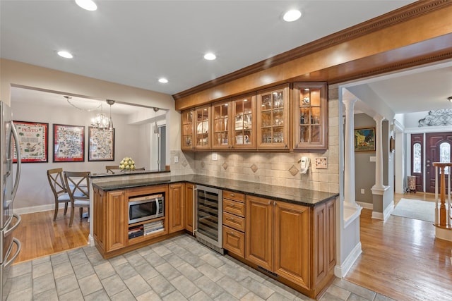 bar featuring an inviting chandelier, decorative columns, stainless steel appliances, wine cooler, and backsplash