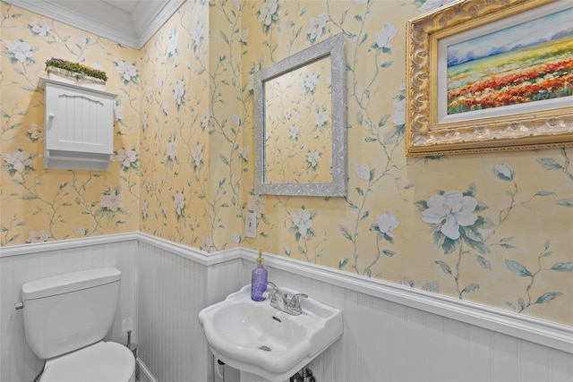 half bathroom with wallpapered walls, toilet, a sink, and wainscoting