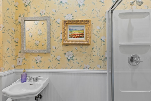 full bath featuring a sink, a wainscoted wall, a stall shower, and wallpapered walls