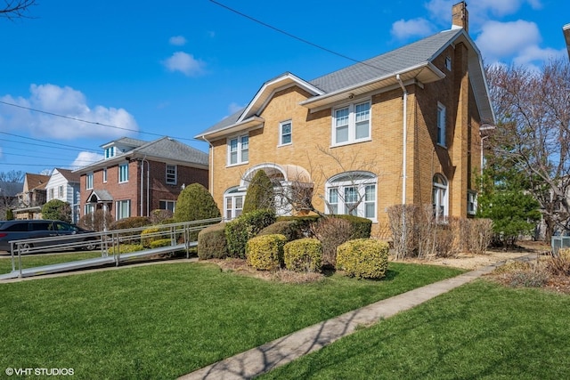 view of front facade with a front yard, brick siding, and a chimney