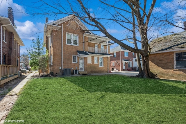 rear view of property featuring cooling unit, brick siding, a chimney, and a lawn