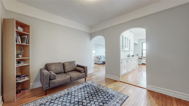 living area with arched walkways, light wood-style flooring, and baseboards