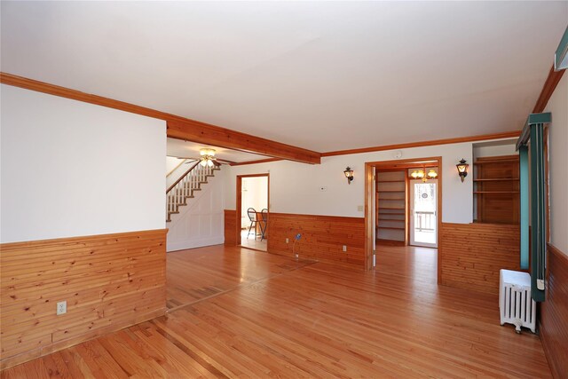 unfurnished living room featuring light wood-type flooring, radiator, a wainscoted wall, and stairway