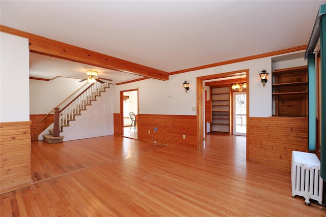 unfurnished living room featuring ornamental molding, stairway, wainscoting, radiator, and light wood finished floors