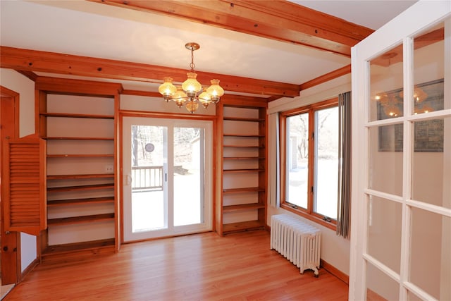 unfurnished dining area with light wood-style floors, radiator, a healthy amount of sunlight, and a chandelier