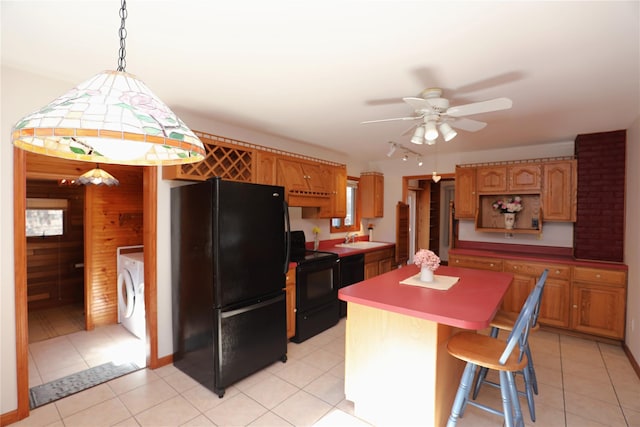 kitchen featuring light tile patterned floors, washer / clothes dryer, a kitchen island, a sink, and black appliances