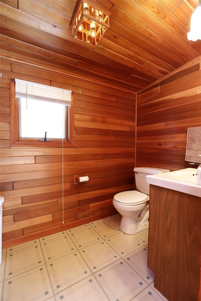 half bathroom with toilet, wood walls, wood ceiling, vanity, and tile patterned floors